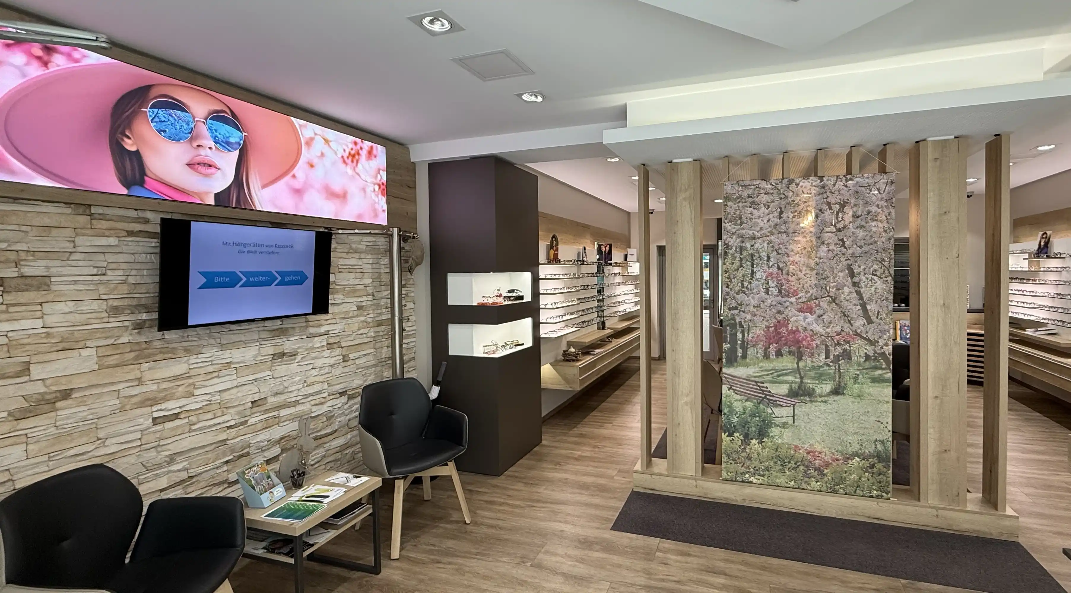 Wartebereich im Optiker-Geschäft mit Brillenregalen, Stühlen und Display.