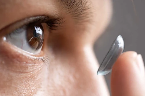 Nahaufnahme eines Auges, vor dem eine Person eine Kontaktlinse mit der Fingerspitze zum Einsetzen hält.